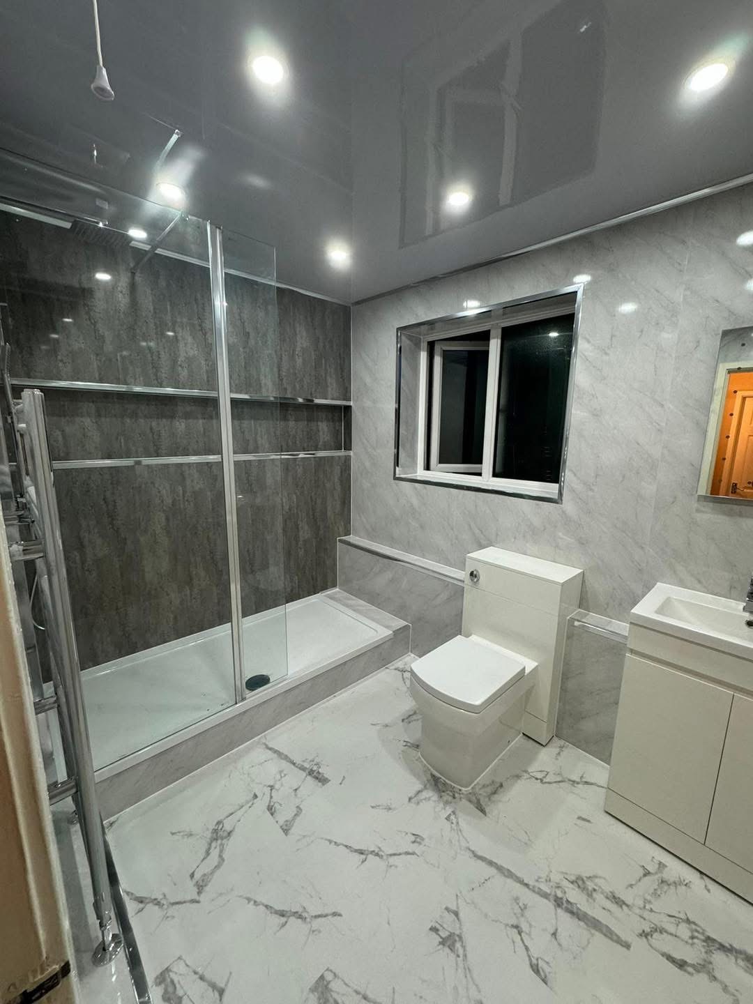Bathroom with a glazed shower enclosure, WC, vanity basin and marble-effect wall and floor finishes.