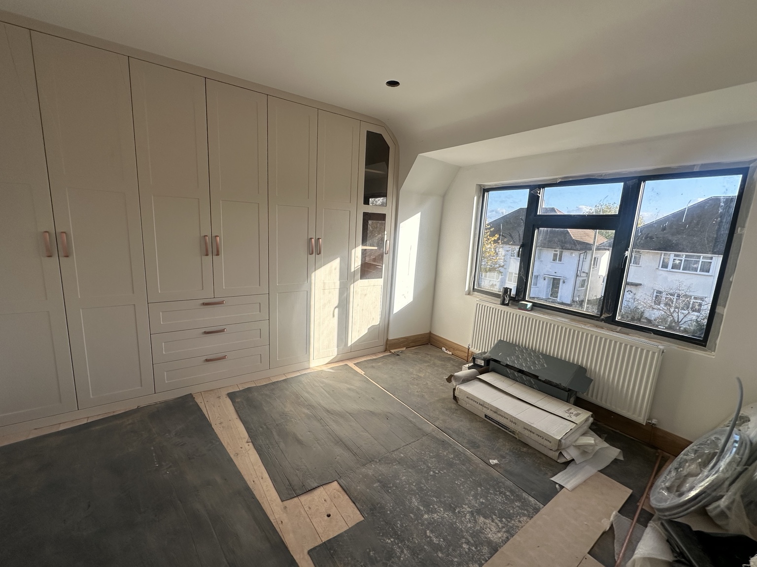 Fitted bedroom wardrobes and flooring installation in progress, with new skirting and a radiator below the window.