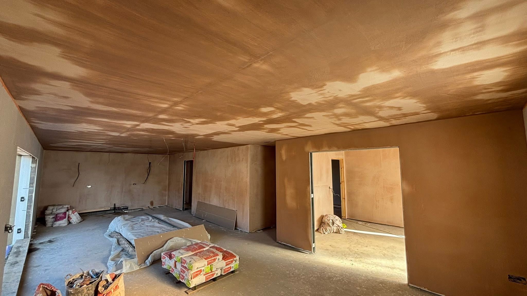 Freshly plastered walls and ceiling in a large interior, with materials and electrical cables visible during renovation.