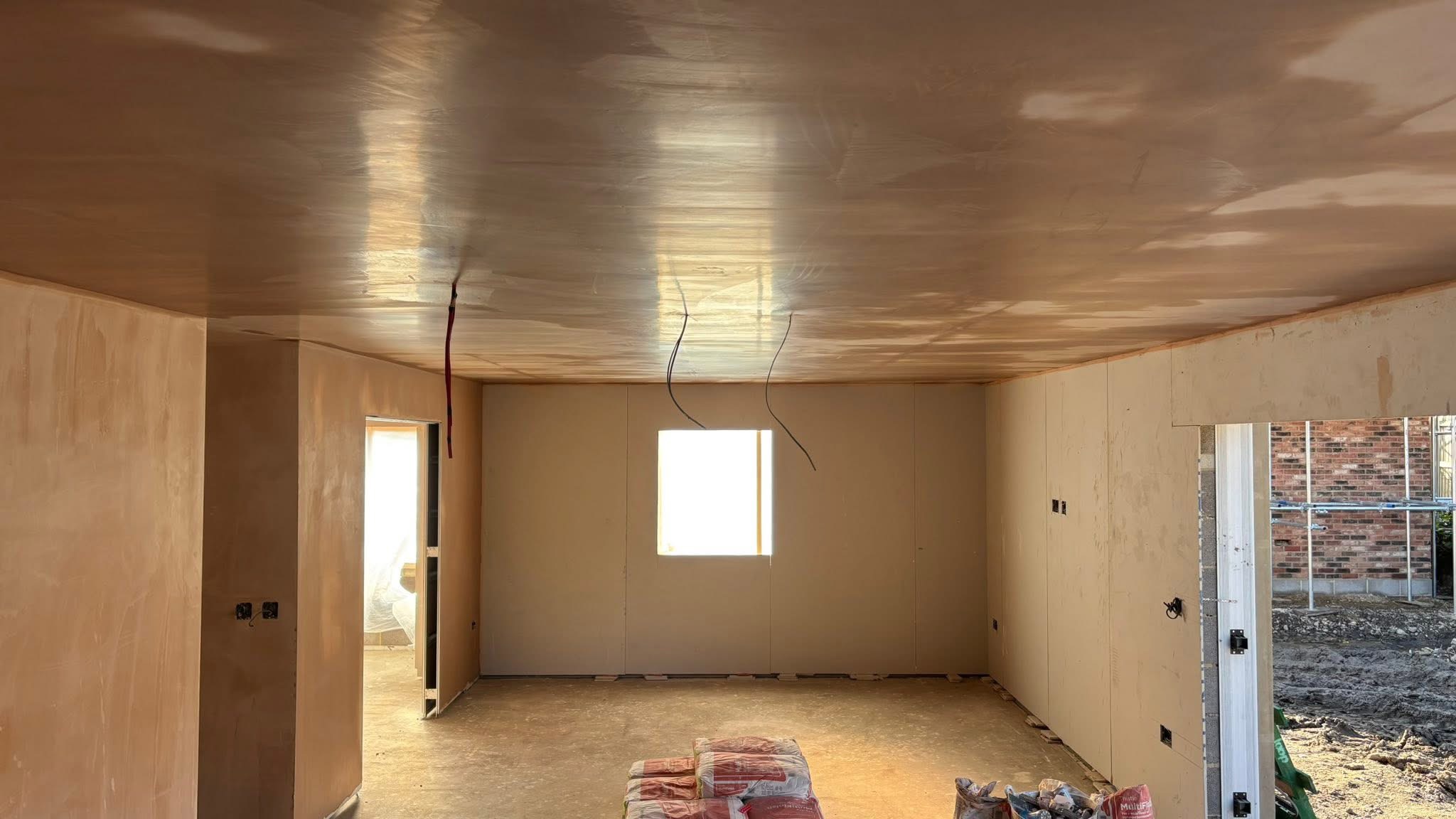 Plaster skimming to walls and ceiling around new door and window openings, with first-fix electrical cables visible.