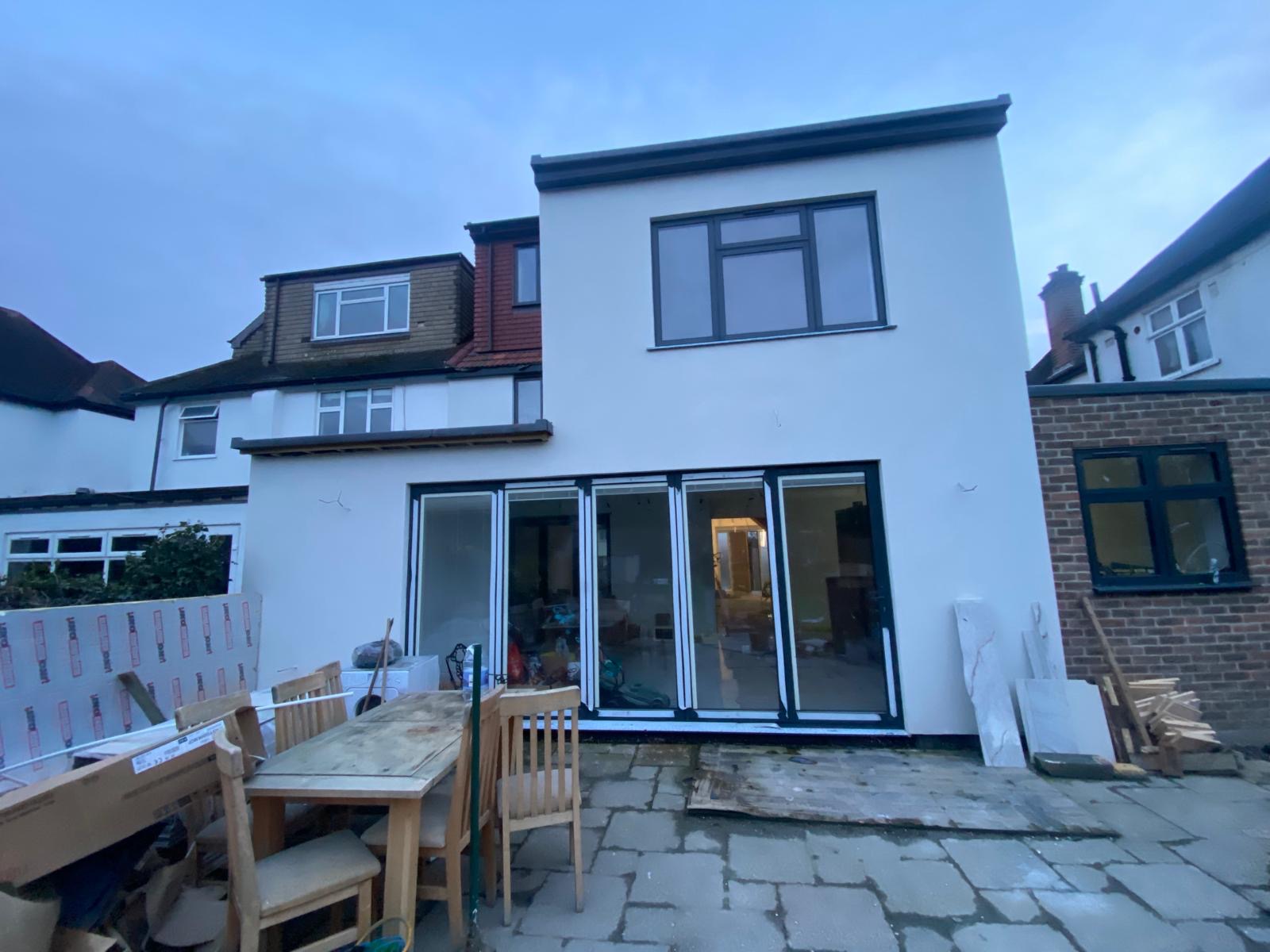Rear house extension with white render, upper-floor window and glazed folding doors during finishing work.