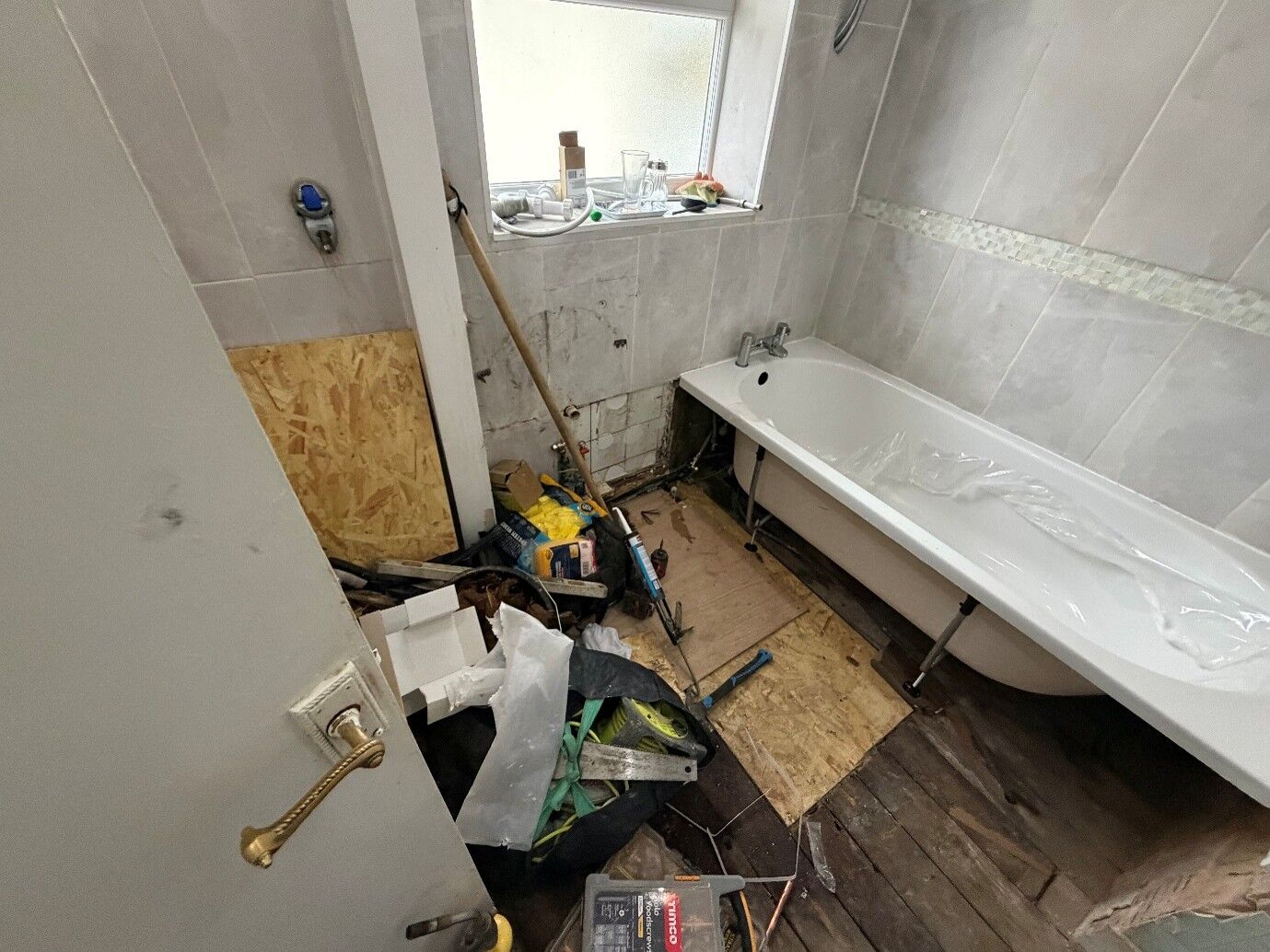 Bathroom during strip-out, with the old bath, tiles and floorboards coming out