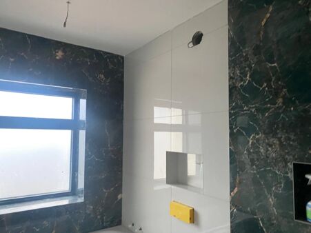 Bathroom wall tiling in large white gloss tiles with dark green marble-effect feature tiles