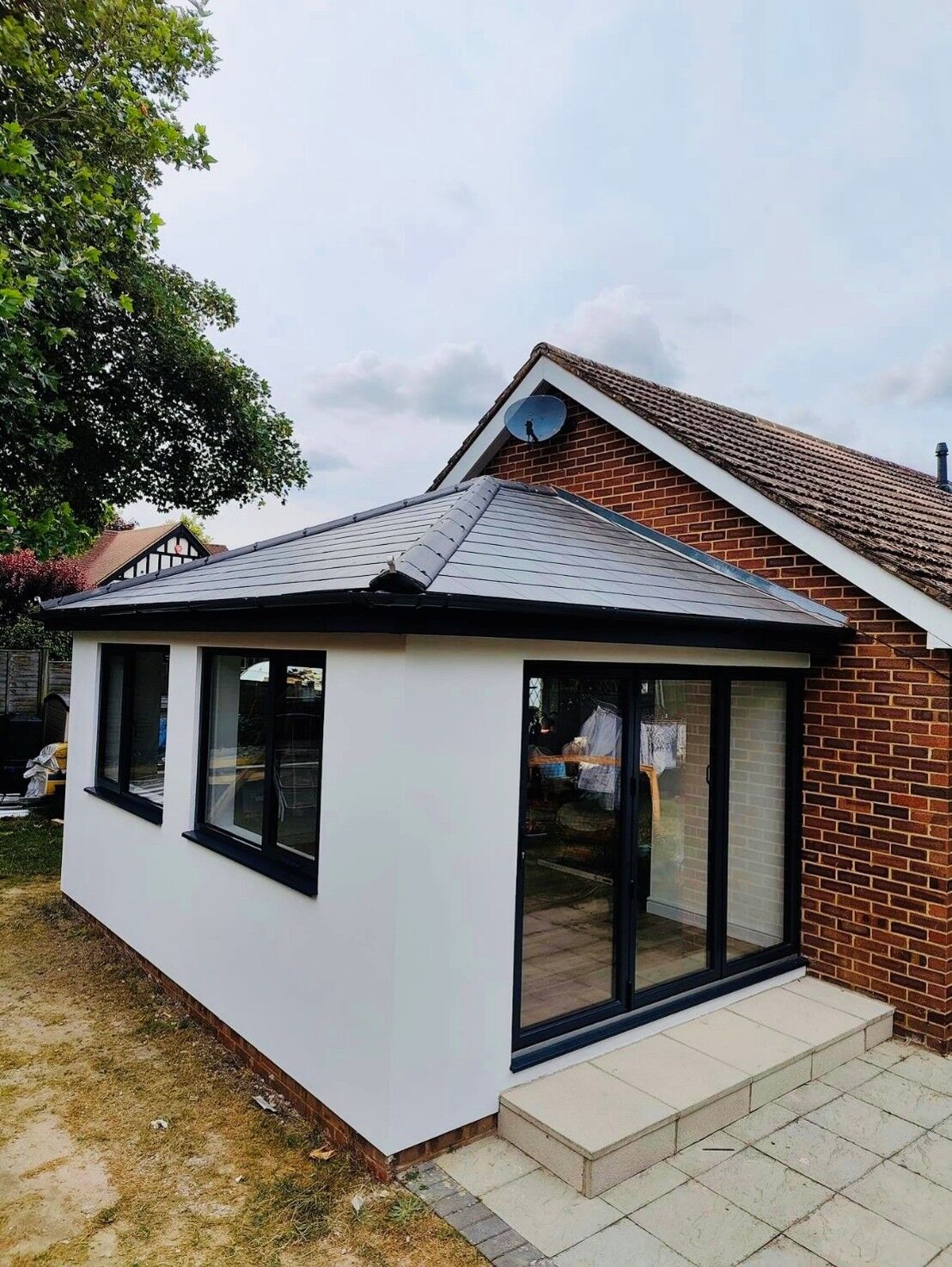 White rendered garden room with a slate-effect roof and black-framed sliding doors